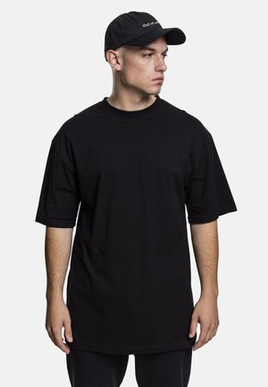 T-shirt nera oversize con maniche corte e scollo rotondo, realizzata in tessuto di cotone. Indossata con un cappello nero con scritte bianche.