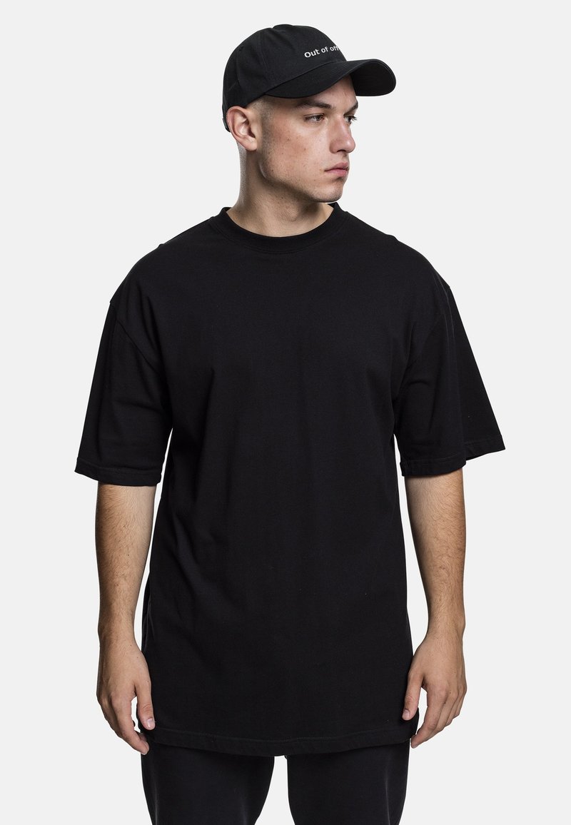 T-shirt noir surdimensionné à manches courtes et col rond, en tissu de coton. Porté avec une casquette noire ornée de texte blanc.