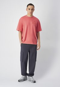 Koraalkleurig oversized t-shirt met een bedrukte logo, gecombineerd met donkerblauwe cargobroek met zijzakken. Grijze sportschoenen maken de look af.