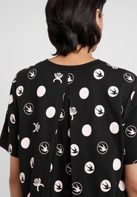Czarny bawełniany T-shirt z mieszanką różowych wzorów w kształcie okręgów i ilustracji, z centralnym zakładką na plecach dla dodatkowego efektu designerskiego.
