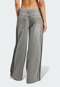 Jeans de denim gris de pierna ancha con franjas laterales negras, diseño de cinco bolsillos y un ajuste relajado. Textura desteñida con un dobladillo limpio.