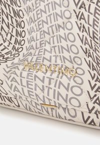 Vadderad handväska med ett ljusbeige yttre och ett upprepat grått "VALENTINO"-mönster. Guldfärgade metalldetaljer. Slät textur.