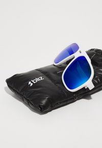 Weiße Sonnenbrille mit blauen Verlaufslinsen, die auf einem schwarzen gepolsterten Etui mit einem weißen Logo ruht. Das Design ist kantig und sportlich.