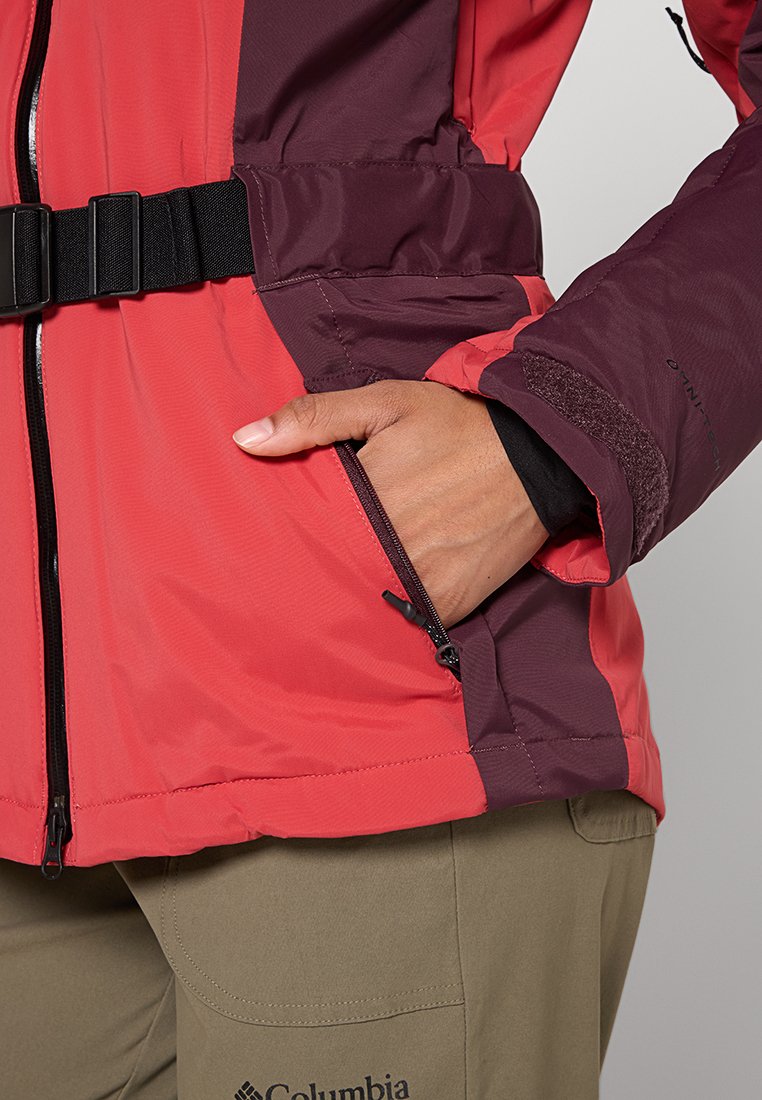 Rote und bordeauxfarbene wasserdichte Jacke mit hohem Kragen, verstellbarem Taillenbund und mit Reißverschluss ausgestattetem Taschen auf der linken Seite.