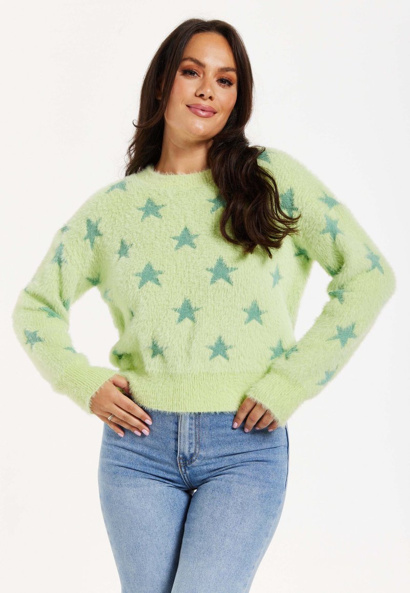 Green fuzzy sweater with a star pattern in light blue. Features long sleeves and a ribbed hemline, worn with light blue jeans.