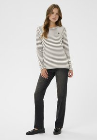 Prúžkovaná košeľa s dlhým rukávom v krémovej a hnedej farbe, s okrúhlym výstrihom; kombinovaná s tmavými džínsami a čiernymi mokasínami. Minimalistický dizajn, bez vzorov.