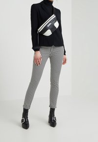 Musta bleiseri mustan poolopaitatakin päällä, yhdistettynä musta-valkoviirullisiin housuihin ja polven ylle ulottuviin mustiin saappaisiin. Mukana on musta-valkoinen olkalaukku.