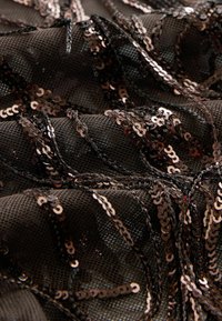 Tissu en mesh noir orné de sequins noirs et bronze brillants disposés en motifs ondulés et superposés.