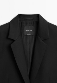 Zwarte op maat gemaakte blazer met notch-reverkraag en binnenlabel met de tekst Massimo Dutti, gemaakt in Portugal.