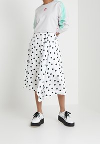 Felpa grigia corta con strisce verde menta, gonna midi a pois bianchi e scarpe con plateau con lacci neri e tomaia bianca.