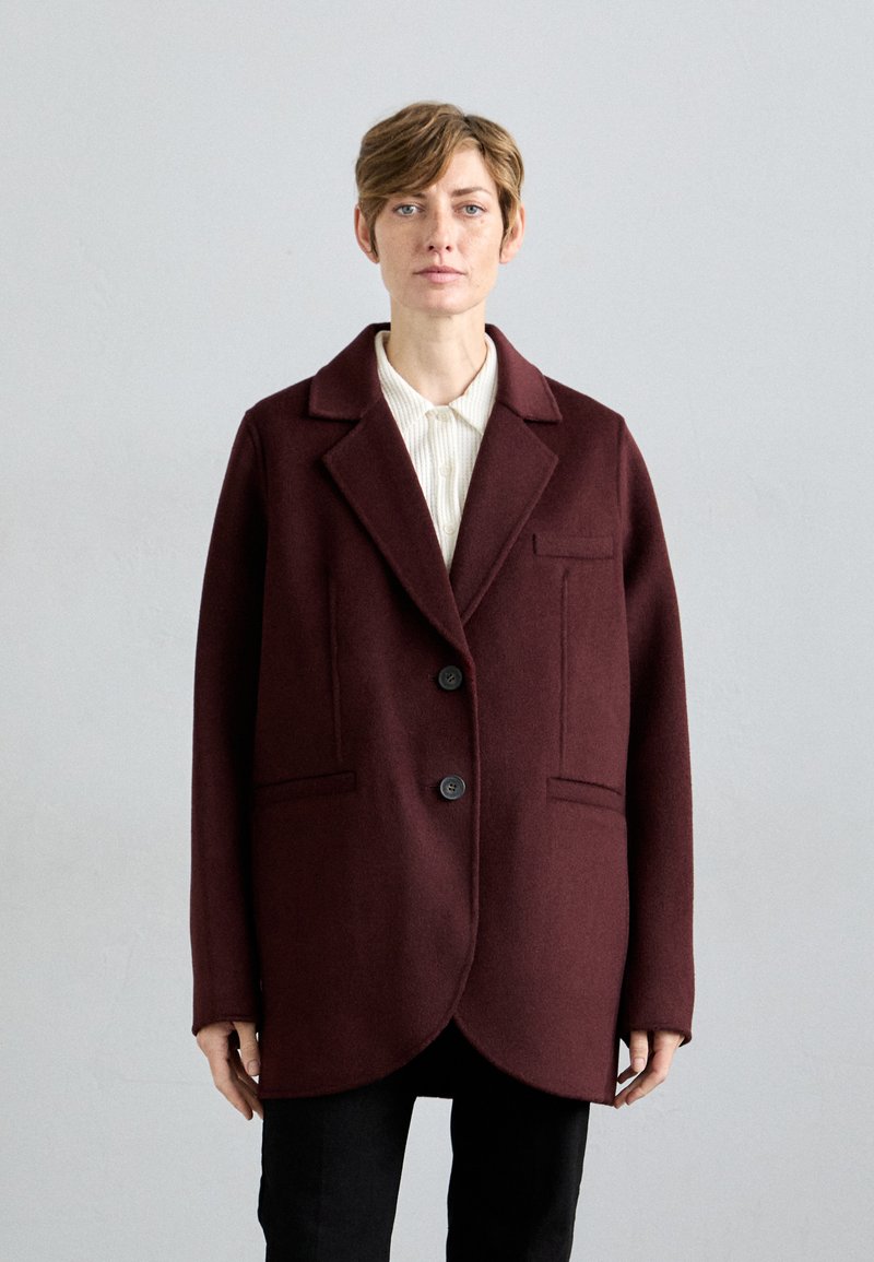 Cappotto in lana bordeaux con colletto a revers, due tasche anteriori e due bottoni. Presenta una texture liscia e morbida e un orlo arrotondato.