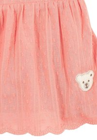 Falda rosa coral hecha de una tela suave, con puntos en relieve, dobladillo con forma de olas y un bordado de cara de oso en la parte frontal.