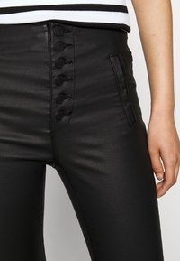 Czarne, dopasowane spodnie wykonane z gładkiego materiału, w wysokim stanie, z ozdobnymi guzikami i boczną kieszenią.