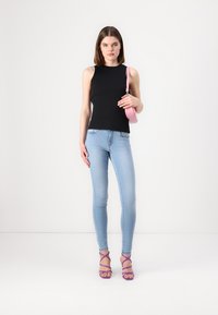 Black sleeveless top, light blue skinny jeans, and purple strappy heels. Pink handbag held in right hand. Simple, fitted silhouette.