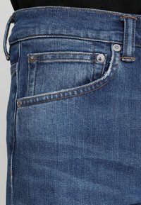 Niebieskie dżinsy z klasycznym pięciopocketowym wzorem, kontrastowym przeszyciem, metalowymi elementami i lekko wyblakłym wykończeniem.