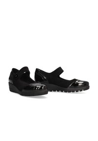 Zapatos negros con una punta de charol texturizado, cuerpo de ante y un leve tacón en cuña. Cuentan con una correa de velcro para un ajuste seguro.