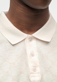 Ανοιχτό ροζ πόλο πουκάμισο με υφασμάτινο ανάγλυφο σχέδιο, γιακά και πατιλέτα με τρία κουμπιά. Μαλακό, απαλό ύφασμα με διακριτική λάμψη.