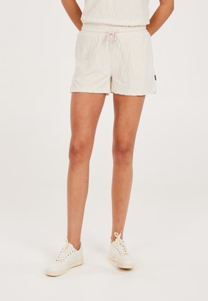 Femme portant un short crème texturé avec cordon de serrage et des baskets assorties, debout devant un fond clair uni.