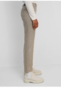 Pantalon à carreaux beige et marron, coupe slim, taille mi-haute avec poches latérales, assorti à des bottines beige.