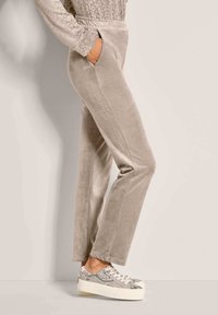 Hellbeige Velourhose mit Seitentaschen, schlanker Passform und glatter Textur, kombiniert mit gemusterten grauen Sneakers mit weißer Sohle.