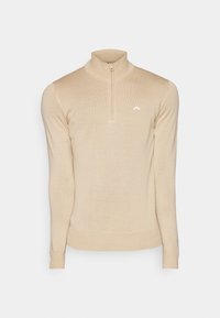 Beige ribbad tröja med hög krage och halvdragkedja, med långa ärmar och en vit logotyp på bröstet. Slät tygkänsla.