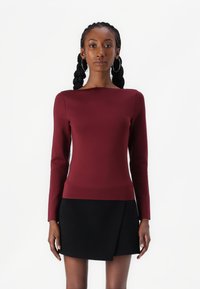 Haut bordeaux à manches longues avec un col bateau, design ajusté, texture unie, et une jupe noire en A avec un détail drapé.