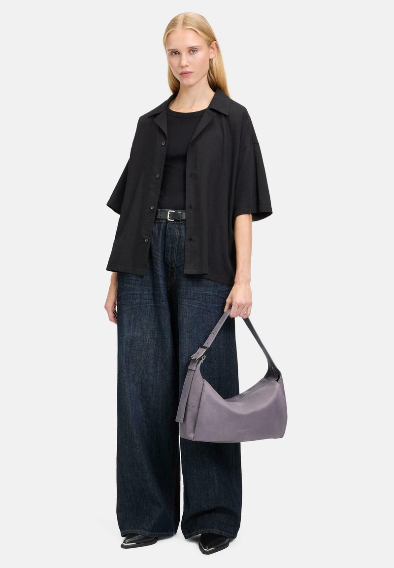 Schwarzes, oversized Hemd, enges schwarzes Top, weit geschnittene, dunkelblaue Jeanshose und graue Ledertasche mit schickem Design und Tragegurt.