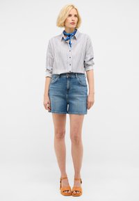 Shorts de mezclilla de tiro alto, de lavado azul y con un diseño clásico de cinco bolsillos, combinados con una camisa de botones a rayas blancas y azules.