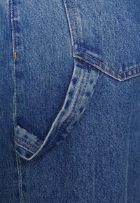 Jeans de denim con un lavado azul claro, que presentan costuras naranjas en contraste y un detalle visible en el bolsillo trasero. Textura suave con áreas desgastadas.