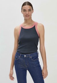 Marineblauwe tanktop met een roze geribbelde halslijn, met een getailleerd ontwerp. Gecombineerd met donkere spijkerbroeken. Soepele textuur en minimale details.