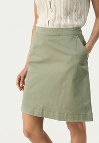 Kaki grön A-linjeformad kjol i ett mjukt, lätt material, med sidofickor och en rak nederkant med diskreta sömnadsdetaljer.