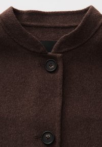 Donkerbruine wollen jas met een ronde kraag en twee grote zwarte knopen op de voorklep.