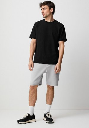 Camiseta negra de manga corta con textura combinada con pantalones cortos grises, que presentan una cintura elástica. Zapatillas deportivas negras y calcetines blancos hasta el tobillo completan el conjunto.