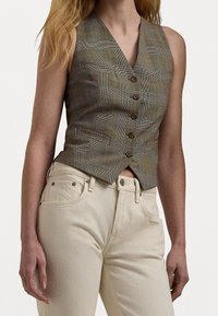 Grå rutig väst med en figursydd design, med fem bruna knappar, djupa fickor och en skarp V-ringning. Tillsammans med högmidjade beige jeans.