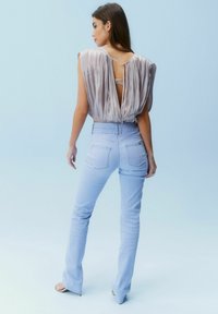 Top sans manches, plissé, en gris clair avec un dos en keyhole ; associé à un jean ajusté, taille basse, bleu clair. Tissu lisse et léger brillant.