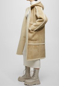 Beige hættejakke med en blød, tekstureret overflade og cremefarvet kant. Kombineret med knæhøje beige snørebodder med en kraftig sål.