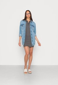 Casaco de ganga em azul claro, vestido cinza com gola e sandálias de slide em creme. Texturas suaves e design casual, vista em comprimento total.
