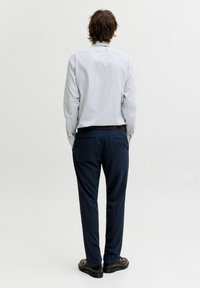 Triibuline helesinine-valge pika varrukaga särk koos tumesiniste pükstega. Kingad on tumedad, jämeda tallaga. Puhas, viimistletud siluett.