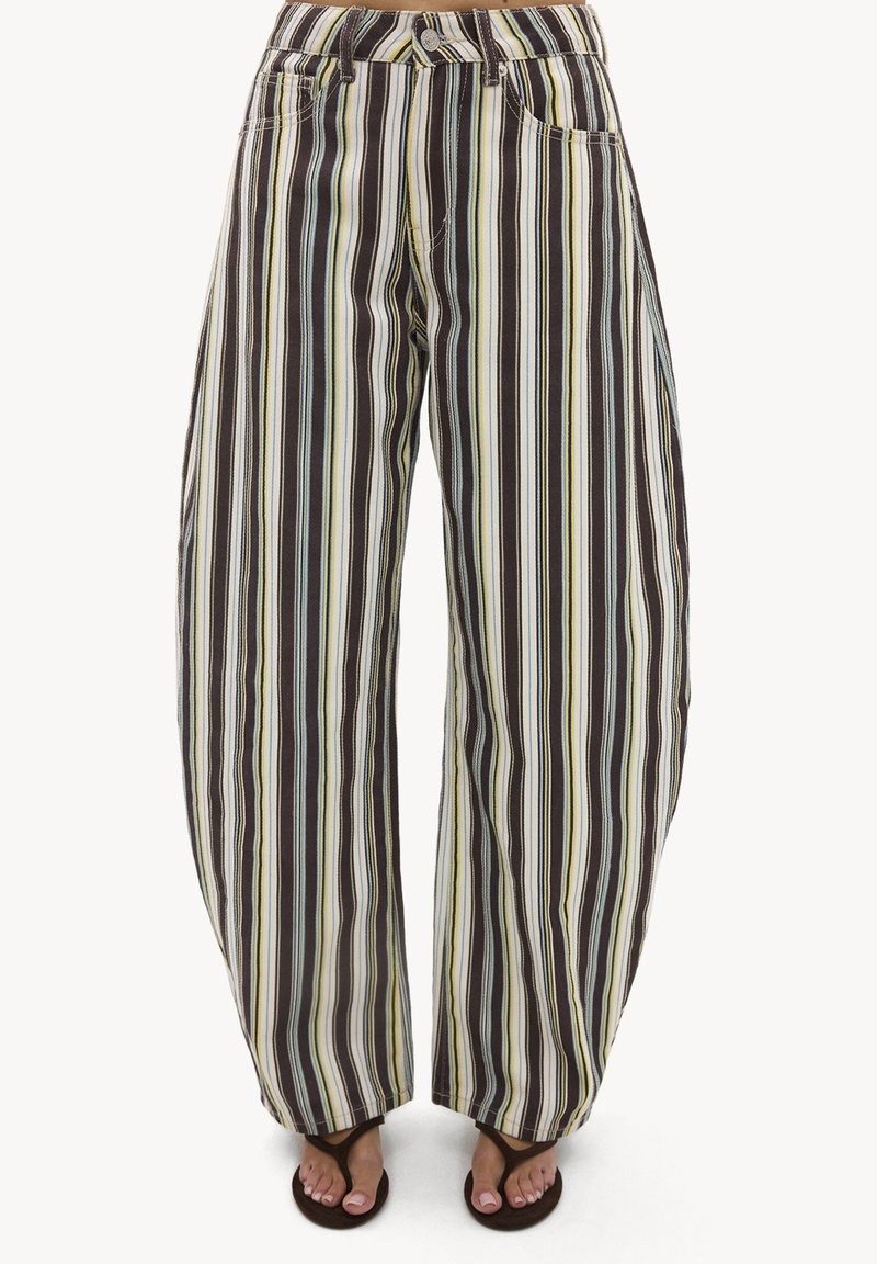 Pantalon à jambes larges avec des rayures verticales dans des tons marron, crème et bleu clair, porté avec des tongs noires et des orteils visibles.