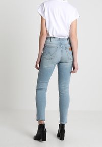 Jeans de tiro alto de color azul claro con una silueta ajustada, que cuentan con bolsillos traseros y una etiqueta de cuero marrón. Combinados con una blusa blanca y botas negras hasta el tobillo.