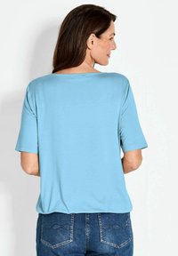 Lichtblauw kortemouwen top met een relaxte pasvorm en een brede halslijn, gecombineerd met donkere spijkerbroek met decoratieve stiksels en zakken.