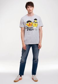 Camiseta de algodón gris con personajes de dibujos animados impresos, Ernie y Bert, en colores negro, amarillo y rojo, con cuello redondo estándar y mangas cortas.