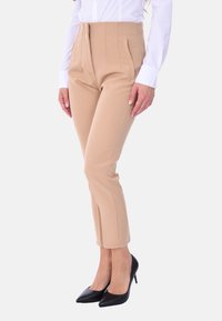 Pantaloni beige a vita alta con tasche laterali, design sartoriale e vestibilità affusolata, abbinati a tacchi neri a punta.