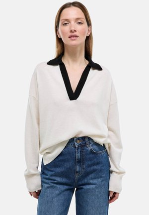 Pull en maille crème avec un col en V profond noir. Comprend des manches longues et des poignets côtelés. Assorti à un jean en denim bleu.