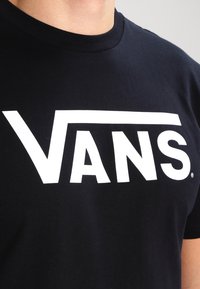 Schwarzes Baumwoll-T-Shirt mit einem großen weißen "VANS"-Logo auf der Brust. Rundhalsausschnitt und kurze Ärmel.