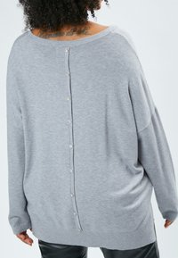 Maglione grigio a maglia con spalle scese, dettagli con bottoni sul retro e polsini a costine. Tessuto morbido, vestibilità rilassata e accenti alla moda con bottoni.