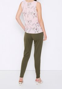 Mouwloze roze bloemen top gecombineerd met olijfgroene taps toelopende broek. De outfit heeft een zachte textuur en een relaxte pasvorm.