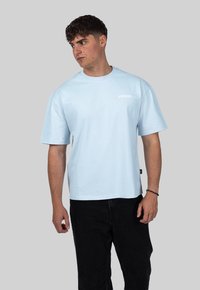 Světle modré tričko s krátkým rukávem a kulatým výstřihem, na přední straně s bílým nápisem "CRYSTAL". V kombinaci s černými kalhotami.