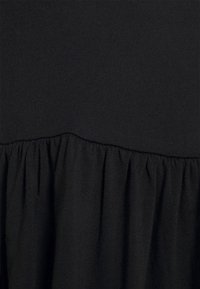 Tissu noir avec une couture froncée divisant une partie supérieure lisse et une partie inférieure texturée et plissée.