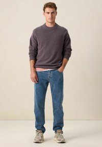 Pull en tricot gris avec un col rond, porté sur une chemise rose pâle, associé à un jean en denim bleu et des baskets beiges. Texture lisse.